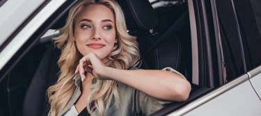 Lächelnde, junge Frau schaut aus dem Fenster ihres Fahrzeugs